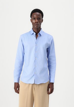 Chemise bleu clair à manches longues avec un col pointu et une patte de boutonnage à l'avant ; texture lisse, coupe ajustée et poignets boutonnés.