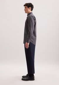 Camicia a maniche lunghe blu navy con un motivo geometrico, abbinata a pantaloni scuri su misura e scarpe in pelle nera, vista di lato.