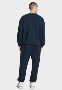 Granatowy zestaw dresowy składający się z bluzy i spodni, wykonany z miękkiego materiału, z luźnym krojem, ściągaczami przy mankietach oraz bocznymi kieszeniami.