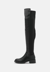 Botas negras por encima de la rodilla hechas de un material de cuero suave con punta redonda y un tacón bajo apilado. Presentan un diseño ajustado.