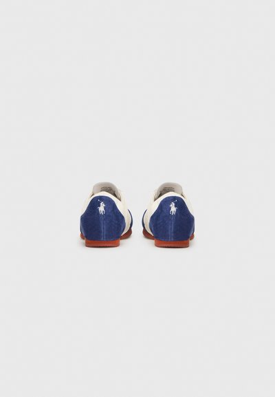 Kék velúr csúszásmentes cipők bézs részletekkel, logóval a saroknál és gumitalppal.