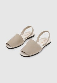 Sandalias slingback beige con los dedos al aire, hechas de cuero suave, con un diseño curvado y una suela de goma negra texturizada.