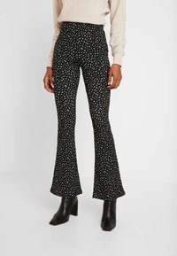 Svarta utsvängda byxor med ett vitt abstrakt mönster, hög midja och en slät yta, i kombination med svarta kängor med blockklack.