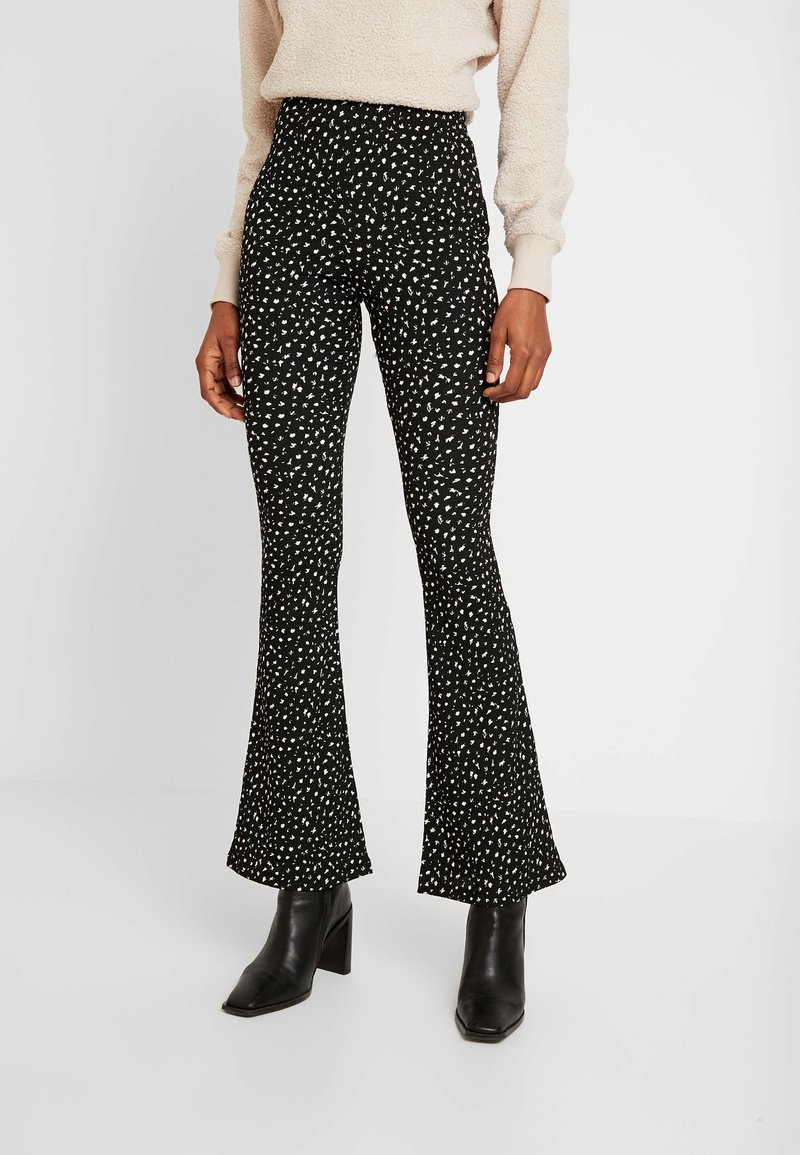 Svarta utsvängda byxor med ett vitt abstrakt mönster, hög midja och en slät yta, i kombination med svarta kängor med blockklack.