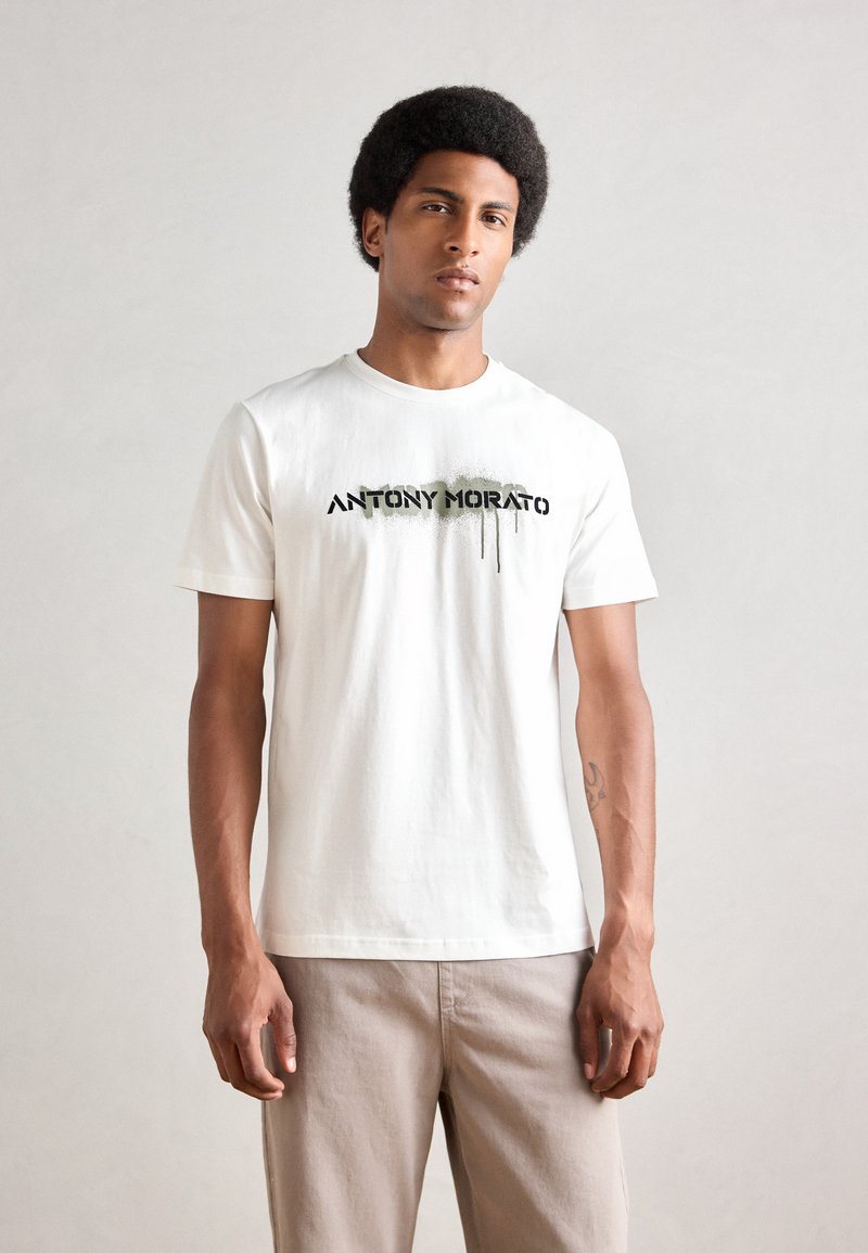 Hvit bomull T-skjorte med et svart og grønt malt logo med dråpeeffekter, crew neck, korte ermer og en avslappet passform.