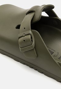 Olivgrønn Birkenstock sandal i slide-modell laget av mykt syntetisk materiale, med en hevet stropp med metallspenne og teksturert fotseng.