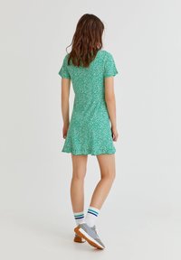 Vestido corto verde con flores, de mangas cortas y dobladillo acampanado. Tejido texturizado, con pequeñas flores blancas, combinado con zapatos grises y calcetines a rayas.