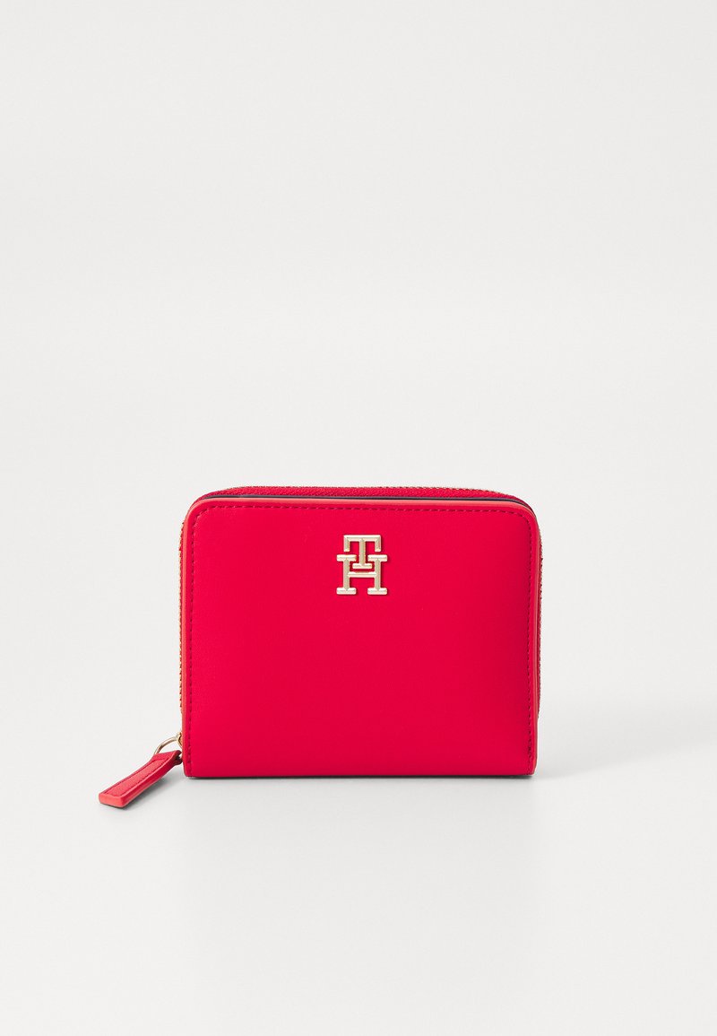 Portefeuille en cuir rouge de forme rectangulaire, avec fermeture à glissière et accent de logo en ton doré. Texture lisse avec un détail de tirette zippée sur le côté.