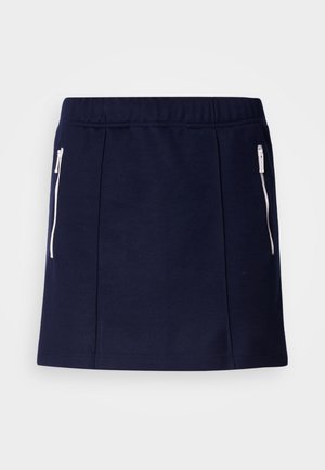 Námořnická modrá sukně vyrobená z měkké látky, která má bílé kapsy se zipem, přiléhavý střih a hladkou texturu. Délka do poloviny stehna.