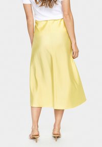 Yellow satin midi skirt featuring a smooth texture, A-line silhouette, and a center back seam. Worn with beige heeled sandals.