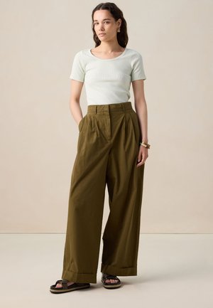 Lichtgroen aangesloten T-shirt met korte mouwen, hoog-waist olijfgroene wijde broek met plooien, zwarte sandalen met gestructureerde zool en bandje.