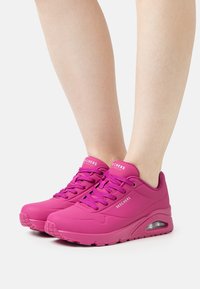 Baskets Skechers roses avec une texture lisse, un design à lacets, des accents perforés et un coussin d'air visible dans la semelle.