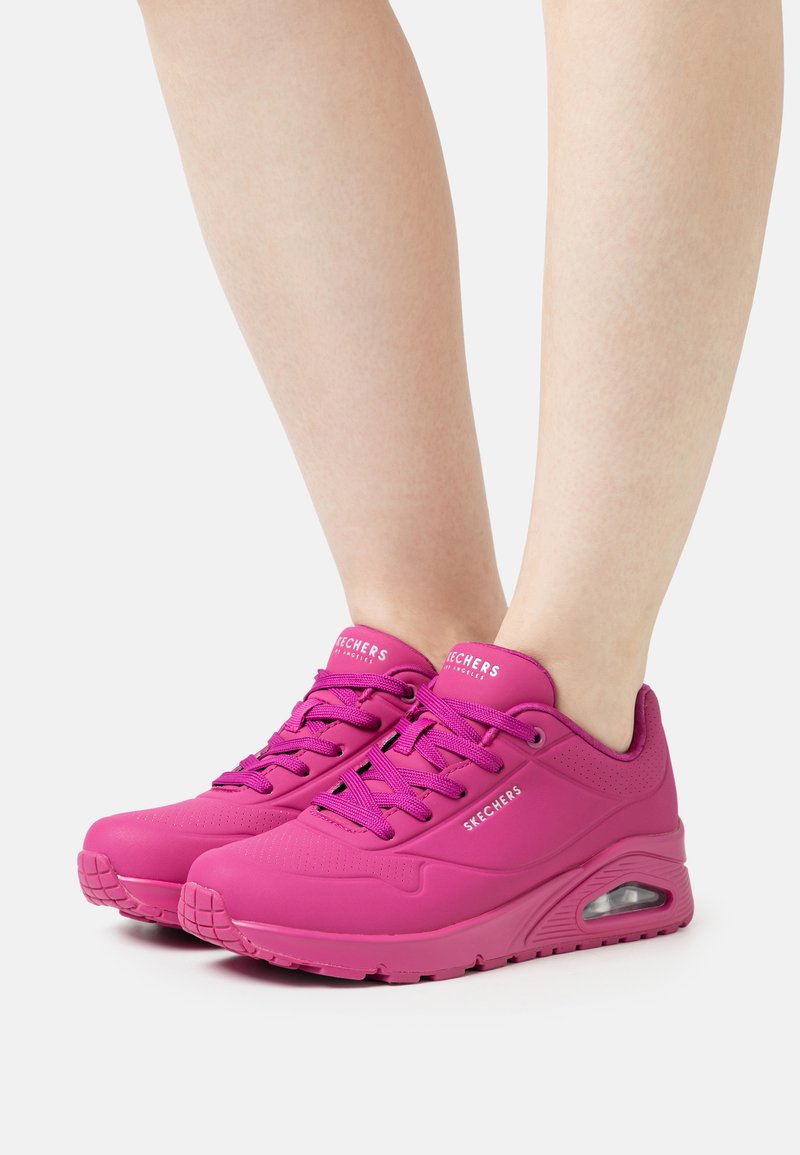 Baskets Skechers roses avec une texture lisse, un design à lacets, des accents perforés et un coussin d'air visible dans la semelle.