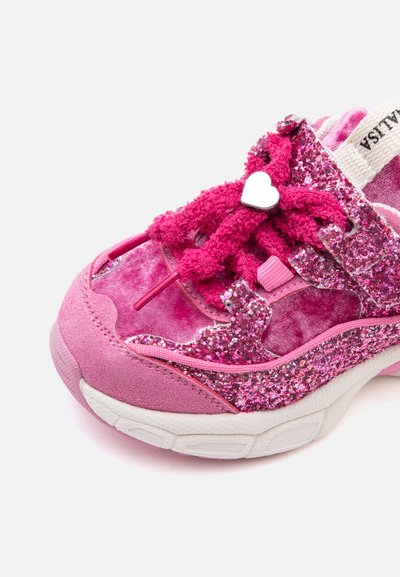 Baskets roses pour enfants avec des détails pailletés, des lacets duveteux noués avec un accessoire blanc en forme de cœur et une semelle blanche sur fond blanc.