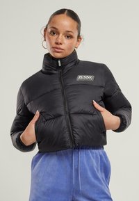 Svart cropped puffer-jakke med høy krage, kviltet design og en sølvlogo-patch. Kombinert med lyseblå velourbukser.