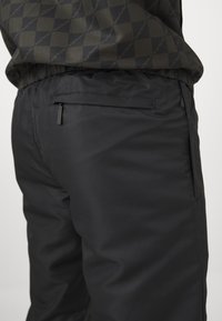 Pantaloni neri con una finitura liscia e strutturata e vita elastica. Presentano una tasca posteriore discreta con chiusura a zip.