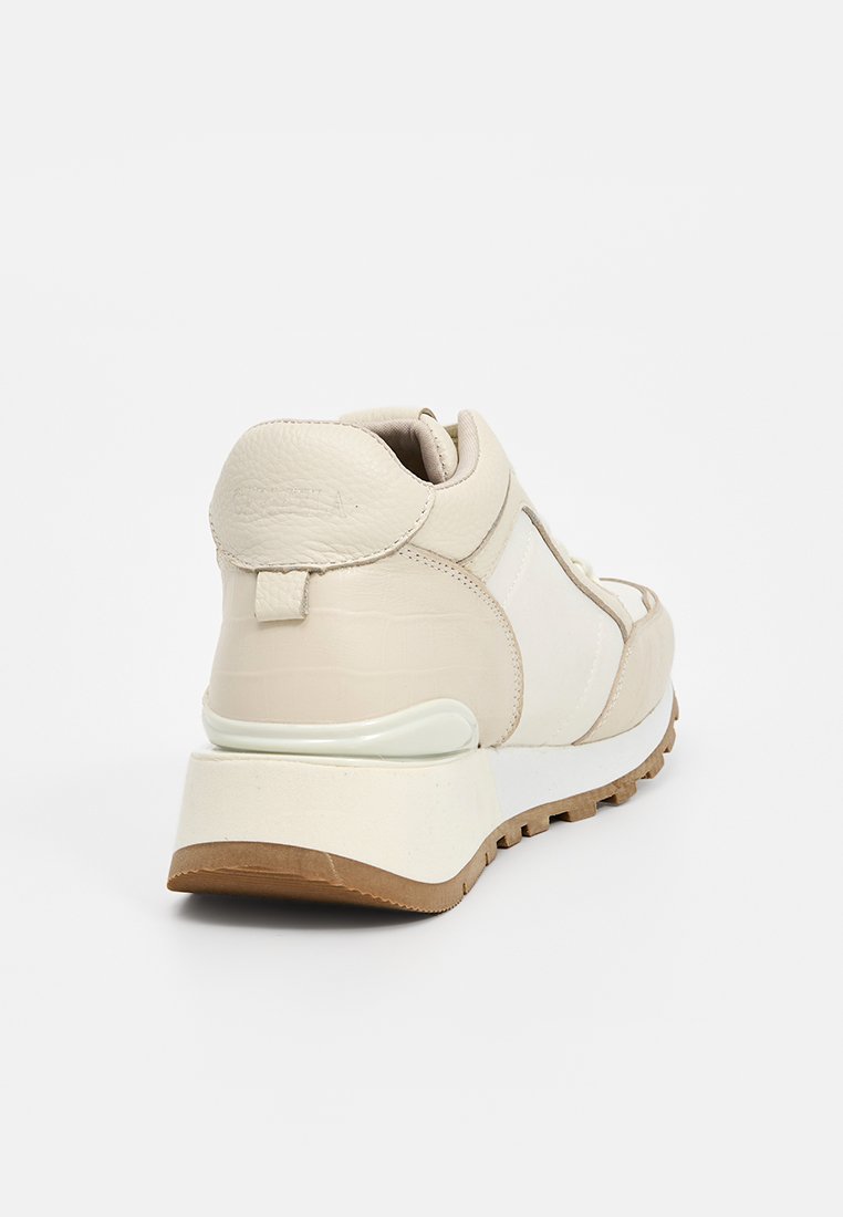 Zapatillas de cuero beige con acentos texturizados, cuello acolchado y suela de goma contrastante. Presenta un diseño moderno y elegante con un branding sutil.