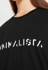 Svart bomulls t-shirt med vit grafisk text "MINIMALISTA". Rund halsringning och korta ärmar, med en mjuk och slät struktur.