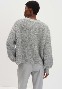 Maglione grigio morbido e textured con una vestibilità ampia, maniche larghe e polsini a coste, abbinato a pantaloni grigi chiari. Design semplice e accogliente.