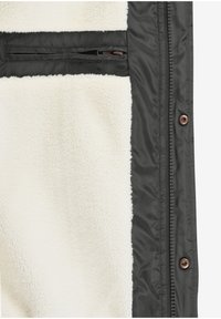 Fleecejacke mit weichem cremefarbenem Innenfutter und schwarzer Außenseite. Verfügt über eine Reißverschlusstasche mit brauner Beschlägen und Druckknöpfen.