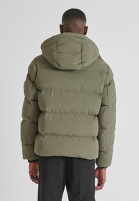 Giubbotto imbottito verde oliva con cappuccio, caratterizzato da un design trapuntato e una finitura liscia e testurizzata. Dettagli di cucitura visibili sulle maniche.