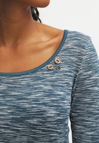 Blått heathered linne med en bred halsringning, prytt med tre dekorativa knappar i olika storlekar, som visar gravyrdesign.