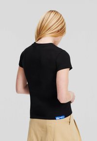 T-shirt nera a maniche corte con design aderente. Caratterizzata da un colletto rotondo e un'etichetta blu di marca sul lato sinistro vicino all'orlo.