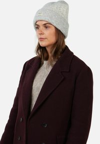Berretto a costine grigio chiaro con risvolto e patch con logo, abbinato a un cappotto doppiopetto bordeaux scuro e a un maglione lavorato a maglia grigio chiaro.