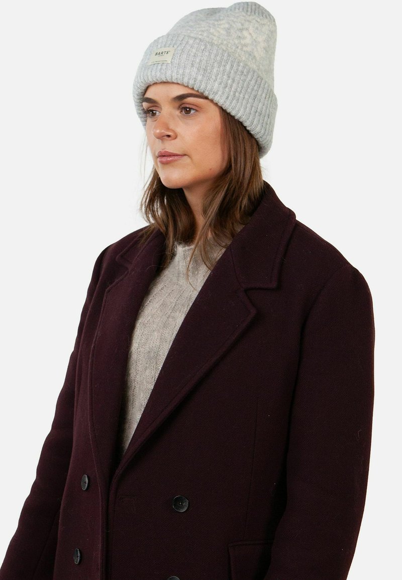 Berretto a costine grigio chiaro con risvolto e patch con logo, abbinato a un cappotto doppiopetto bordeaux scuro e a un maglione lavorato a maglia grigio chiaro.
