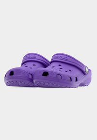 Ζευγάρι μωβ Crocs με οπές αερισμού και ρυθμιζόμενα πίσω λουράκια σε λευκό φόντο.