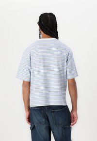 T-shirt de manga corta a rayas en azul claro y blanco, con rayas horizontales y un corte holgado. La tela parece suave y tiene un diseño casual.