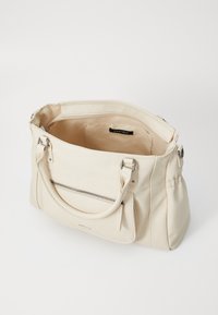 Sac à main beige en matériau lisse, avec deux poignées supérieures, une poche avant zippée et un intérieur spacieux avec étiquette de marque.