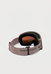 Slēpošanas brillēm ar tonētu lēcu un regulējamu purpura elastīgu joslu, kurai ir tekstūrēti raksti un logo uz vienkārša balta fona.