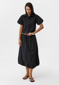 Zwart tweedelig outfit met een cropped knoopshirt met puffmouwen en een hoge taille, knielange rok met een geplooide taille.