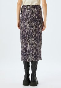 Jupe mi-longue à imprimé animal violet et beige, avec une taille cintrée et une texture douce, associée à des bottes noires jusqu'aux genoux.