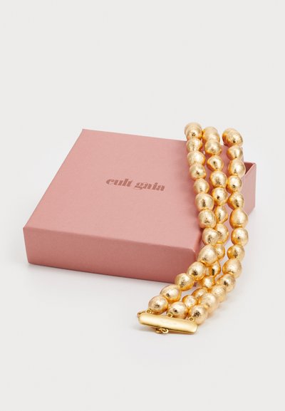 Goldene Perlenarmband mit strukturierten, runden Elementen und einem Verschluss, auf einer rosa Schachtel mit dem Aufdruck "cult gaia" präsentiert.