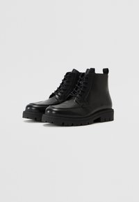 Botas de tobillo de cuero negro con un acabado suave, diseño de cordones, lengüeta en la parte trasera y suela de goma gruesa con dibujo.