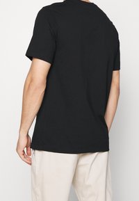 Black cotton t-shirt with short sleeves and a round neckline. Features a straight cut and minimal stitching details on the hem.
