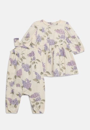Babyoutfit i cremefarve med langærmet top og bukser, dekoreret med mønstre af lilla blomster og grønne blade.