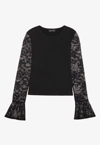 Svart topp med långa ärmar i spets, med en figurnära kropp och utsvängda spetsmuddar. Materialkontrast mellan fasta och genomskinliga texturer.