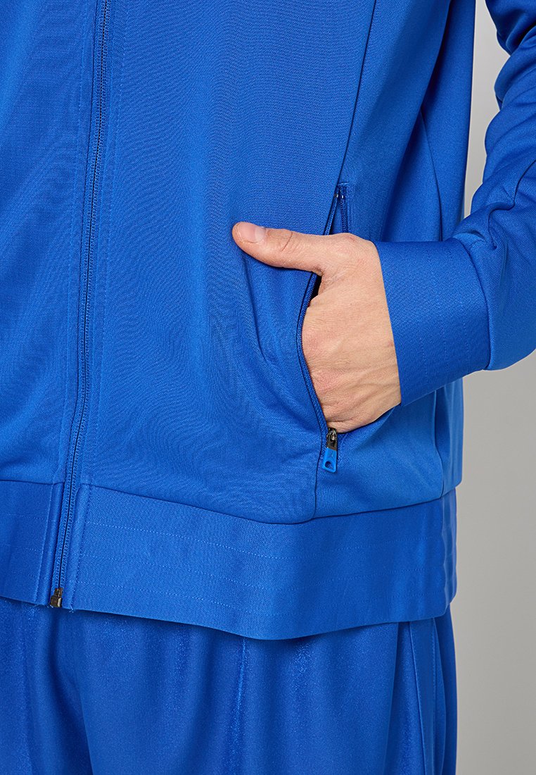 Blue athletic tracksuit with zipper jacket, featuring a side pocket and ribbed cuffs. Smooth texture, fitted design, and durable fabric.