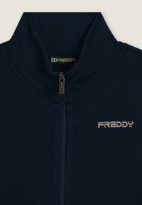 Giacca a zip blu marina realizzata in tessuto morbido, con colletto alto, zip dorata e stampa logo argentata sul lato sinistro.