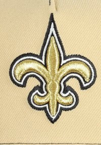 Beiger Stoff mit einem gestickten goldenen und schwarzen Fleur-de-Lis-Logo, das eine detaillierte Textur und einen ausgeprägten Farbkontrast zeigt.