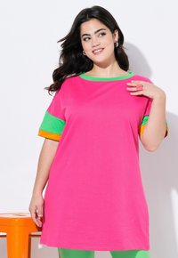 T-shirt surdimensionné rose avec des accents verts, orange et jaunes sur les manches courtes. Texture lisse, encolure arrondie, coupe décontractée.