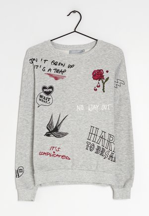 Sudadera gris claro con garabatos negros y rojos y texto que incluye una rosa, un pájaro y frases como "NO CREZCAS ES UNA TRAMPA" y "NO HAY SALIDA."