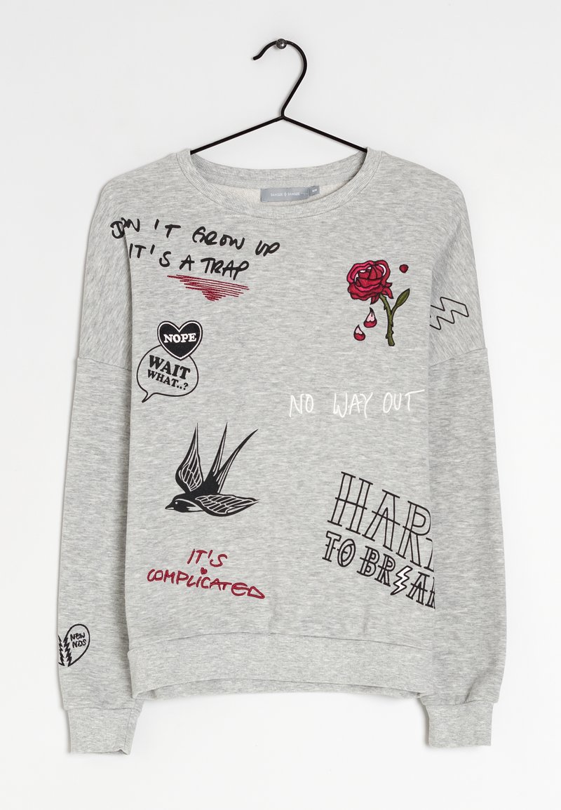 Sweat-shirt gris clair avec des griffonnages noirs et rouges et du texte incluant une rose, un oiseau et des phrases comme "NE GRANDIS PAS, C'EST UN PIÈGE" et "PAS DE SORTIE."