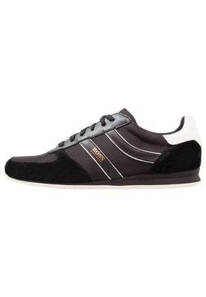 Baskets basses noires avec talon blanc, panneaux en mesh et en suède, lacets, et logo doré "BOSS Hugo Boss" sur le côté.