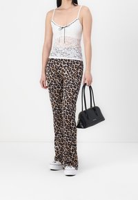 Vit spetslahund med svarta kanter och rosett, kombinerad med bruna byxor med leopardmönster som är utsvängda. Accessoarer inkluderar en liten svart handväska.