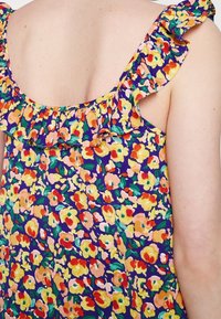Halenka s květinovým potiskem a volánovými ramínky, s fialovým pozadím a multicolorními květinami v žluté, růžové a červené barvě. Lehký materiál.