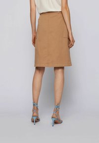 Ruskea puuvillahame, jossa on suora leikkaus ja sivutaskut, yhdistettynä vaaleansinisillä remmikenkiä korkokenkiä. Sujuva rakenne.